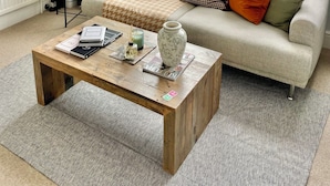 Ein Wohnzimmer mit einer Couch, einem Couchtisch, einer Lampe und großen Fenstern.