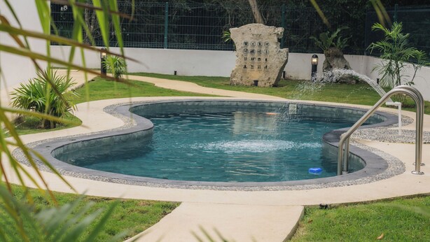 A swimming pool with a stone structure, surrounded by greenery and a fence. - Emma Apartments New with Pool, Jacuzzi, close to the Beach, and playgrounds (Akumal)