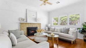 A living room with a fireplace, a sofa, a coffee table, and a large window with blinds. - Pet Friendly - Waves on Rye by Property Mums (Rye)
