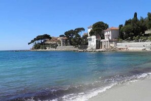Un edificio frente al mar con fachada blanca, ubicado en una playa de arena y aguas azules cristalinas.