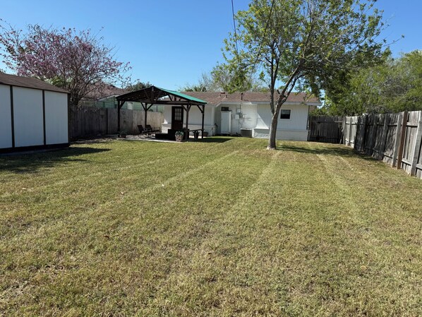 A backyard with a covered patio, a wooden fence, and a small shed. - Port Isabel Home close to SPI Beaches Big Yard, pets Family (Port Isabel)