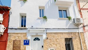 A two-story building with a white facade, numbered 24, featuring a white door, multiple windows, and balconies with plants. - ALMAVERA. Pure Calm House. Colibri 1 Apartment (Madrigal de la Vera)