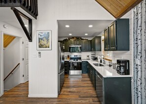 Une cuisine moderne avec un plancher en bois, des appareils électroménagers en acier inoxydable et des meubles de couleur sombre.