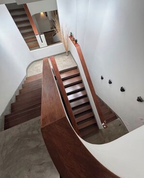 A modern staircase with wooden steps and a curved handrail, leading to a landing with a small plant and wall-mounted light fixtures. - Casa Murciélago🦇Located just off Calle 70-near restaurants and bars. (Medellín)