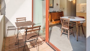 Un patio con tavolo e sedie, una panca in legno e una porta scorrevole in vetro che dà su uno spazio interno con angolo cottura.