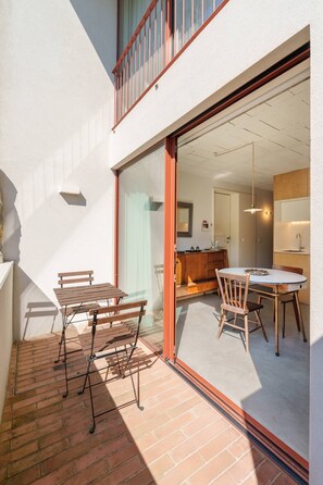 A patio with a table and chairs, a wooden bench, and a sliding glass door leading to an interior space with a kitchen area. - VIVA - Lage Serviced Apartments 29A (Porto)
