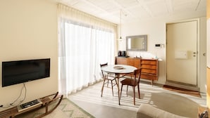 Un soggiorno con TV a schermo piatto, tavolo da pranzo in legno, sedie, un divano, un angolo cottura con forno a microonde e una porta.