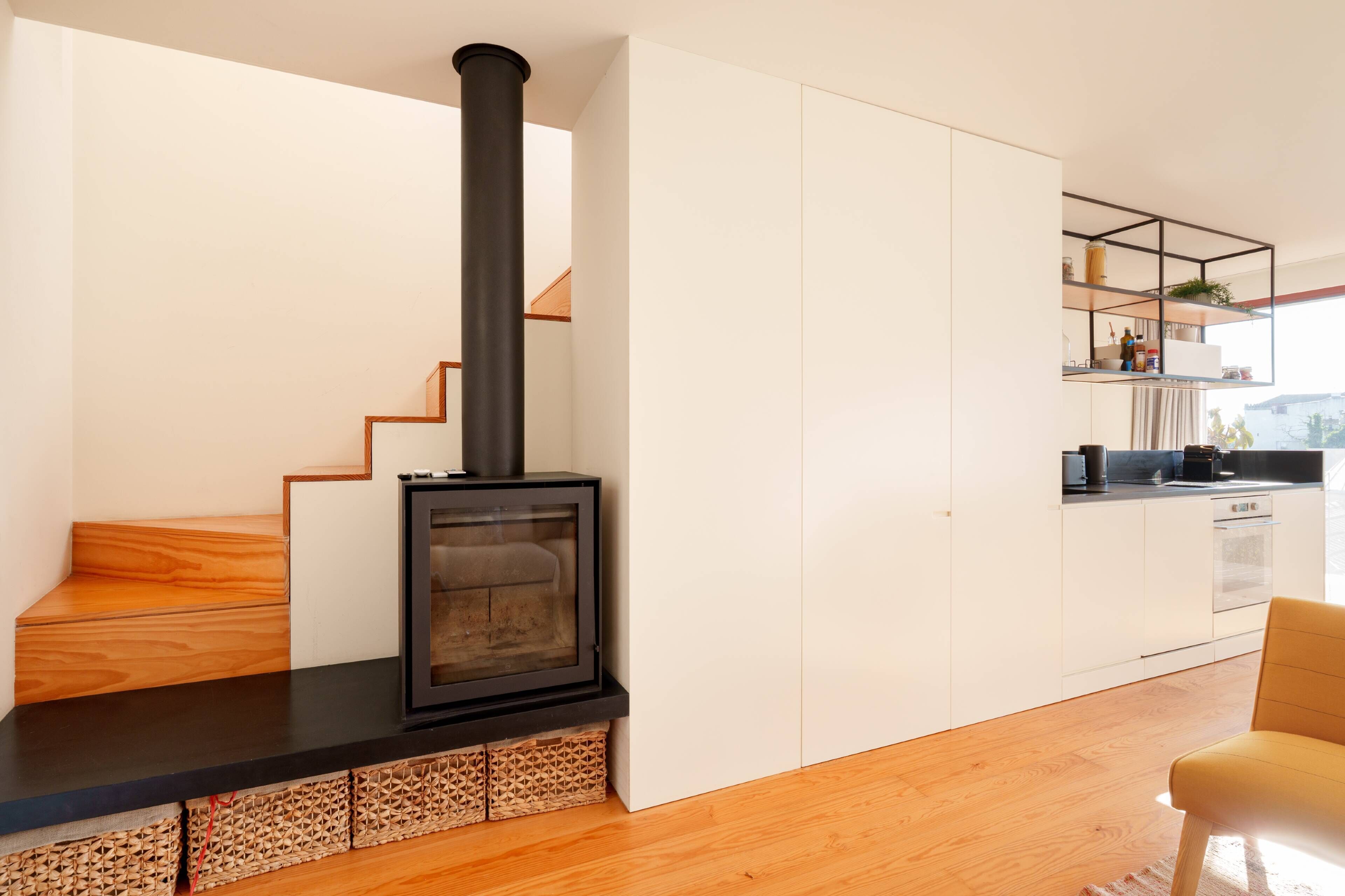 A modern kitchen with a black stove, wooden staircase, and white cabinets.