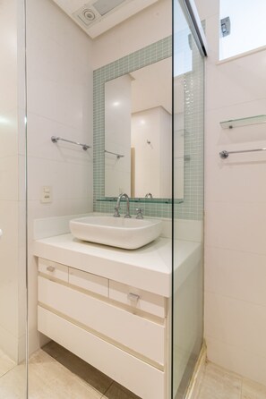 Une salle de bain moderne avec un lavabo entouré de parois en verre, un grand miroir et une étagère en verre.