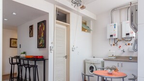 A compact kitchen with a washing machine, a dining area with chairs, and a small table. - Stunning View of Sugarloaf Mountain - Pb1201 (Rio de Janeiro)