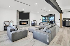 Un salon moderne avec une cheminée, des canapés gris, un téléviseur à écran plat et une vue sur l’extérieur.