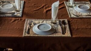 Un espace repas avec des tables dressées pour quatre personnes, chacune agrémentée d’une assiette blanche, de couverts et d’une serviette pliée.