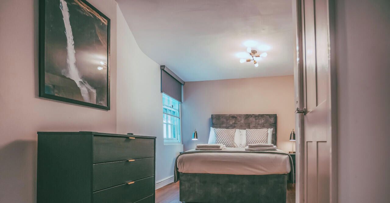 A bedroom with a bed, a dresser, and a painting on the wall.