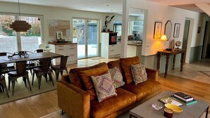 Een moderne woonkamer met een bruine bank, een eethoek met een houten tafel, en een keuken op de achtergrond.