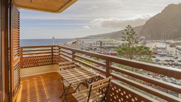 Varanda com guarda-corpo de madeira e vista para o mar e um porto.