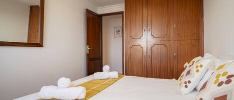 Une chambre d’hôtel avec un lit, une armoire en bois, un miroir et des serviettes.