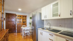 Uma cozinha com armários brancos, geladeira de aço inoxidável, pia e um espaço de jantar com mesa e cadeiras.