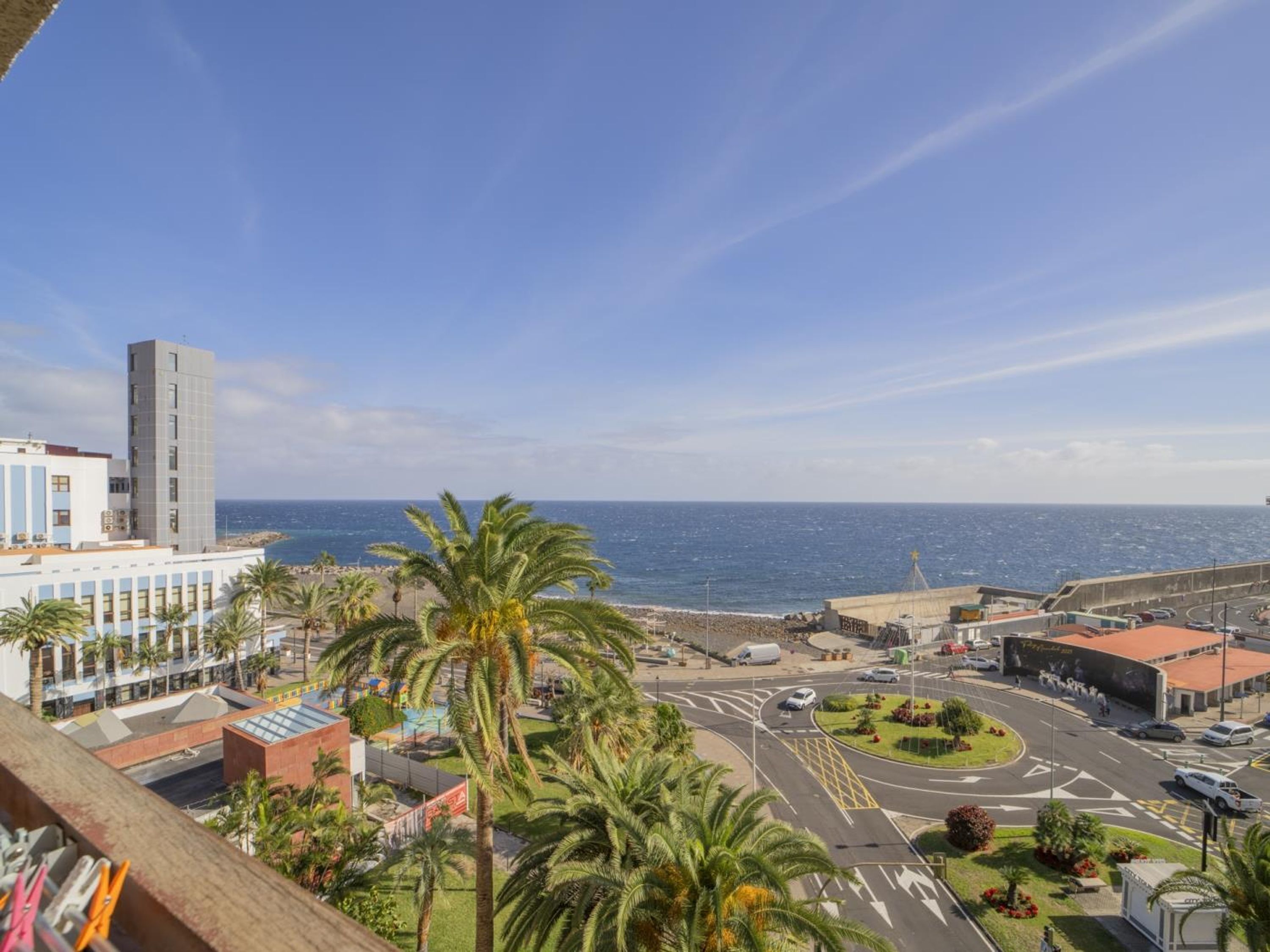 Paesaggio costiero con un edificio importante, palme e vista sul mare.