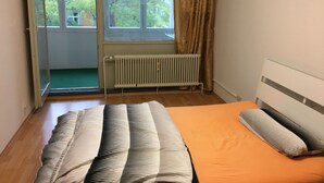 Un dormitorio con cama, un radiador, una ventana con cortinas y vista a árboles fuera.