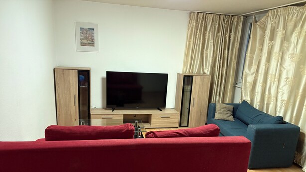 Una sala de estar con televisor, muebles de madera, un sofá azul y cojines rojos.