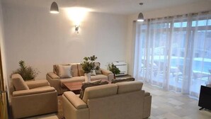 A modern living room with beige sofas, a coffee table, and potted plants. There is a large window with sheer curtains and a view of the outside. - Villa Katarina 5-bedroom near Dubrovnik with private pool (Ivanica)
