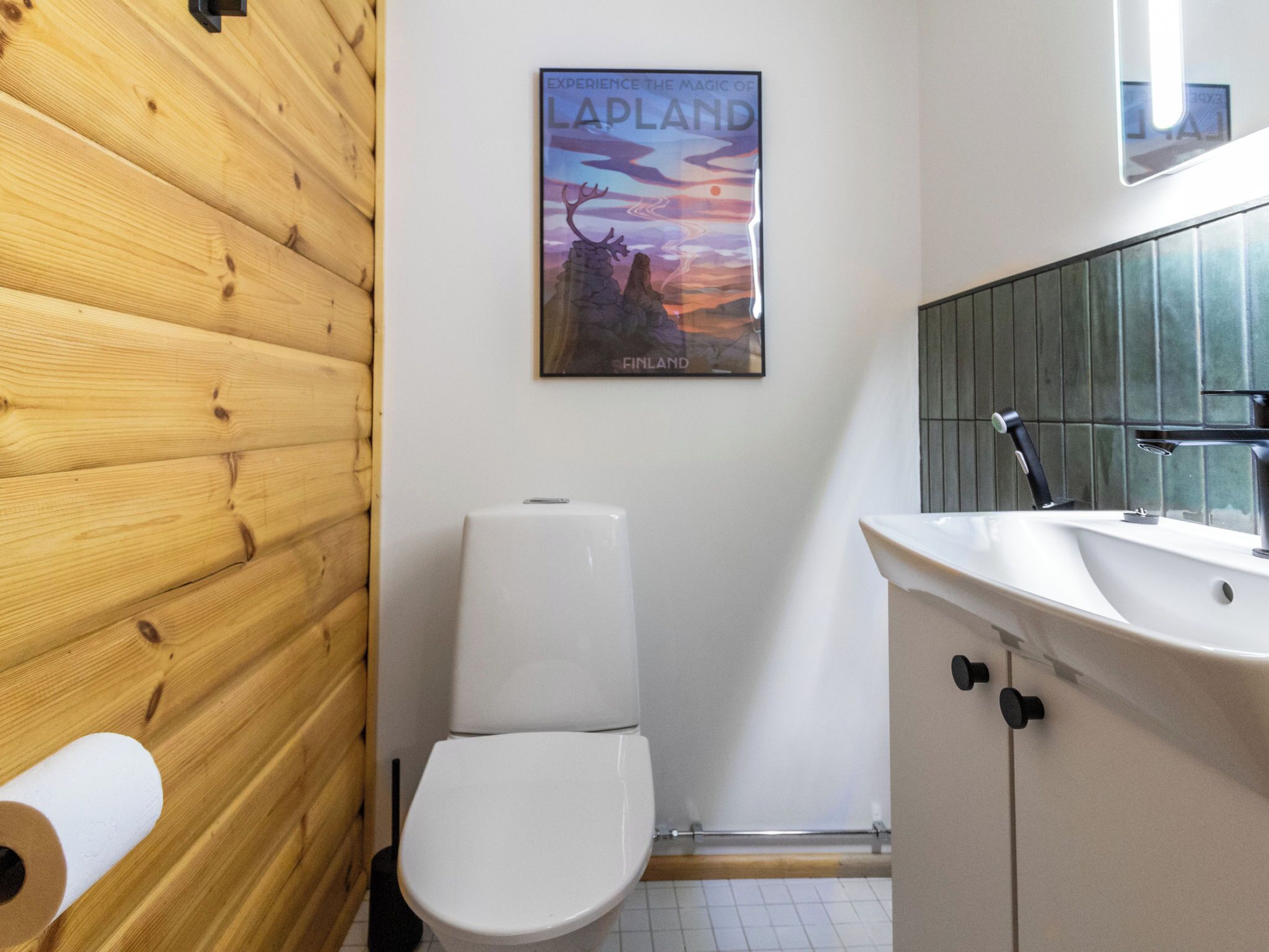 A bathroom with a wooden wall, a toilet, a sink, and a poster of Lapland.