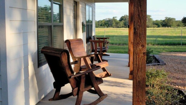 Eine Veranda mit Holzschaukelstühlen und Blick auf ein Wiesenfeld.