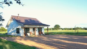Ein eingeschossiges Haus mit Veranda, einem Schotterweg und einem grasbewachsenen Feld im Hintergrund.