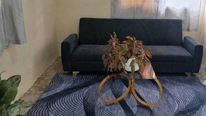 Ein Wohnzimmer mit einem dunkelgrauen Sofa, einem Glastisch mit Pflanze, einem gemusterten Teppich und einem Beistelltisch aus Marmor.