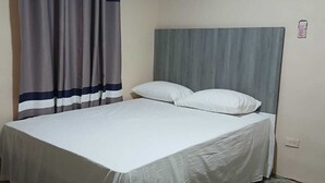 A single bed with a grey headboard, white bedding, and a grey and white striped curtain.
