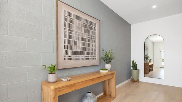 Et moderne interiør med et trækonsolbord, et stort abstrakt kunstværk og et spejl, der reflekterer et rum med en dør og en plante.