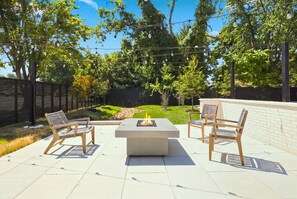 Eine Terrasse im Freien mit einem Feuerbereich, zwei Holzstühlen und einem Tisch.