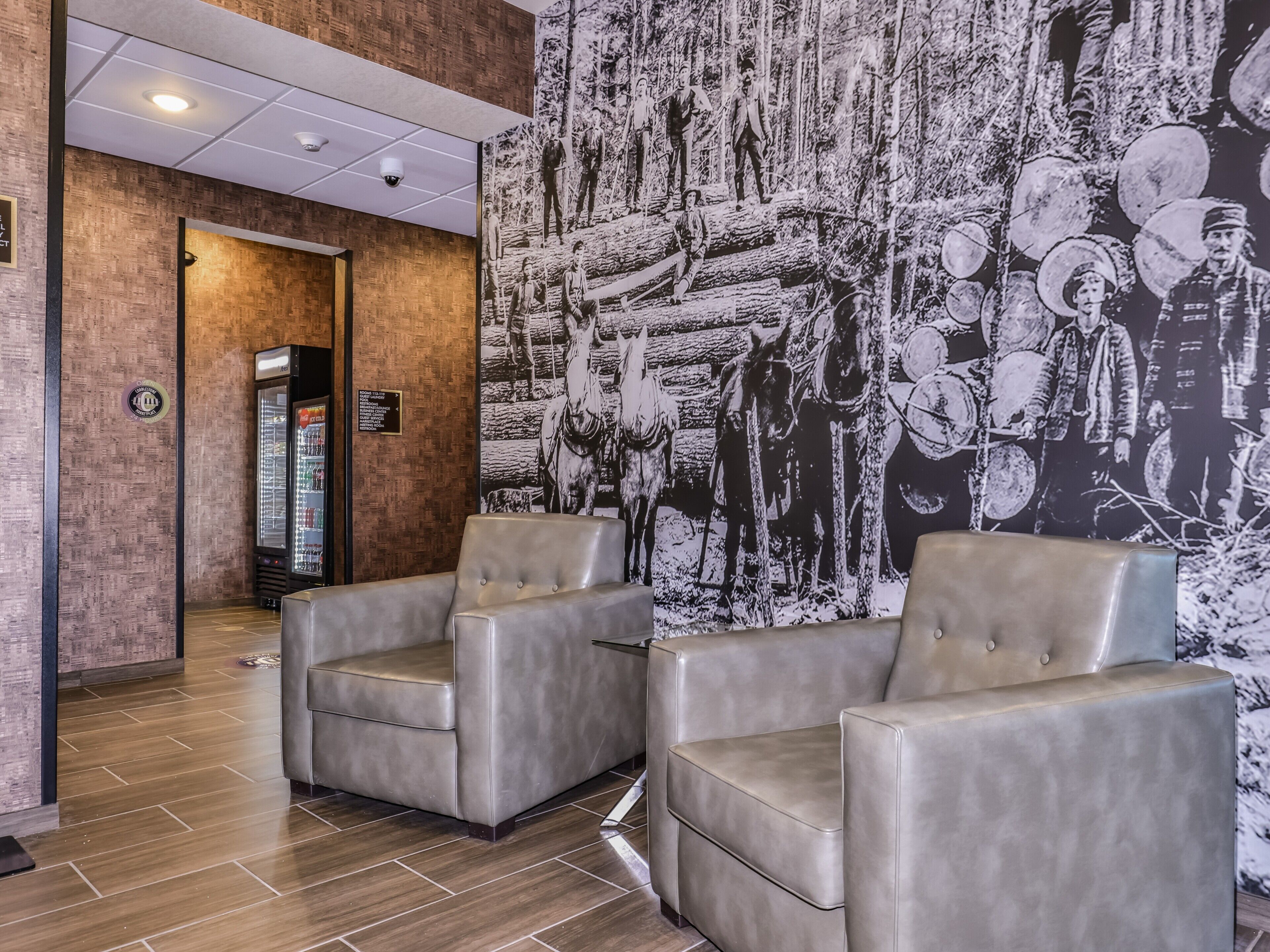 A lobby with two grey leather armchairs, a large black and white mural depicting historical figures, and a modern ceiling with recessed lighting.
