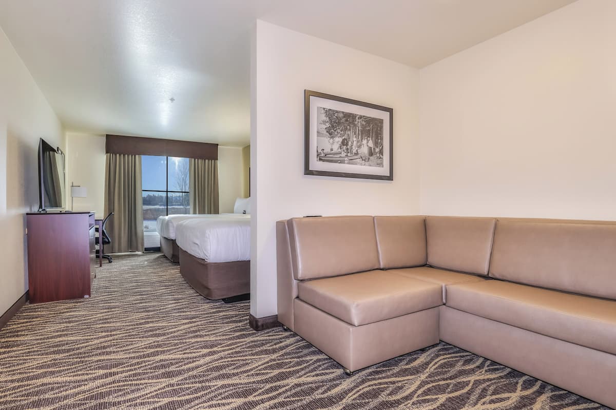Een hotelkamer met een grote beige bank, een bed, een bureau met lamp en een ingelijst schilderij aan de muur.