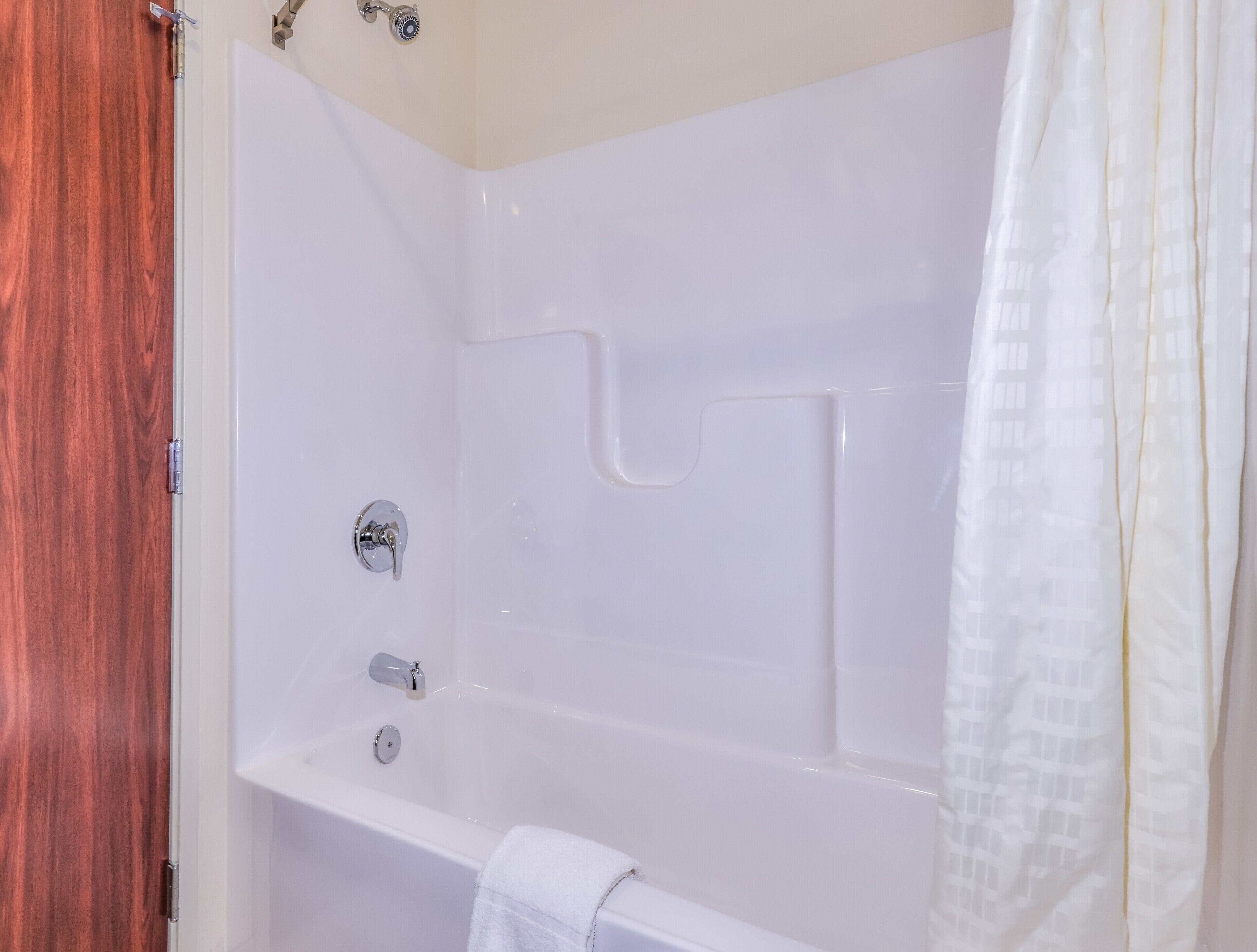 A white bathtub with a shower curtain, a towel, and a wooden door.