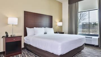 Quarto de hotel com uma cama grande, duas mesas de cabeceira, uma luminária em cada uma, uma janela com cortinas e vista para árvores.