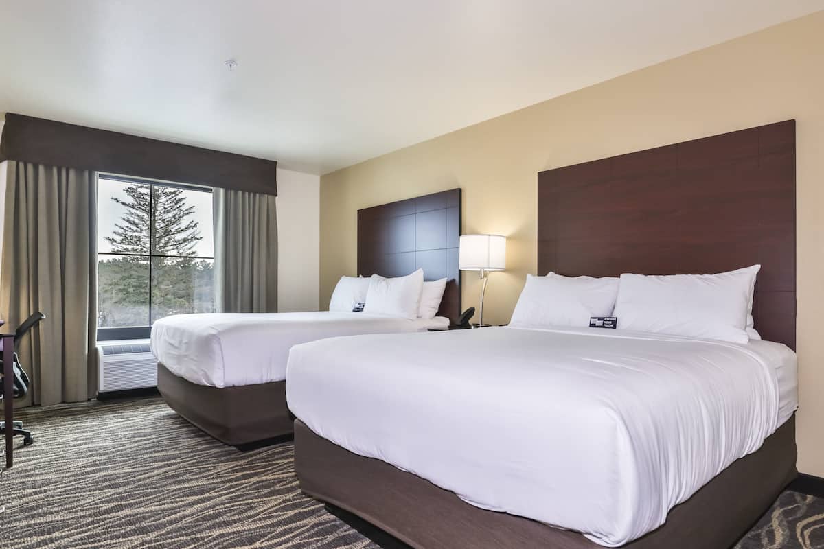 Een hotelkamer met twee bedden, een groot raam met gordijnen, een hoofdbord, een lamp en een tapijtvloer.