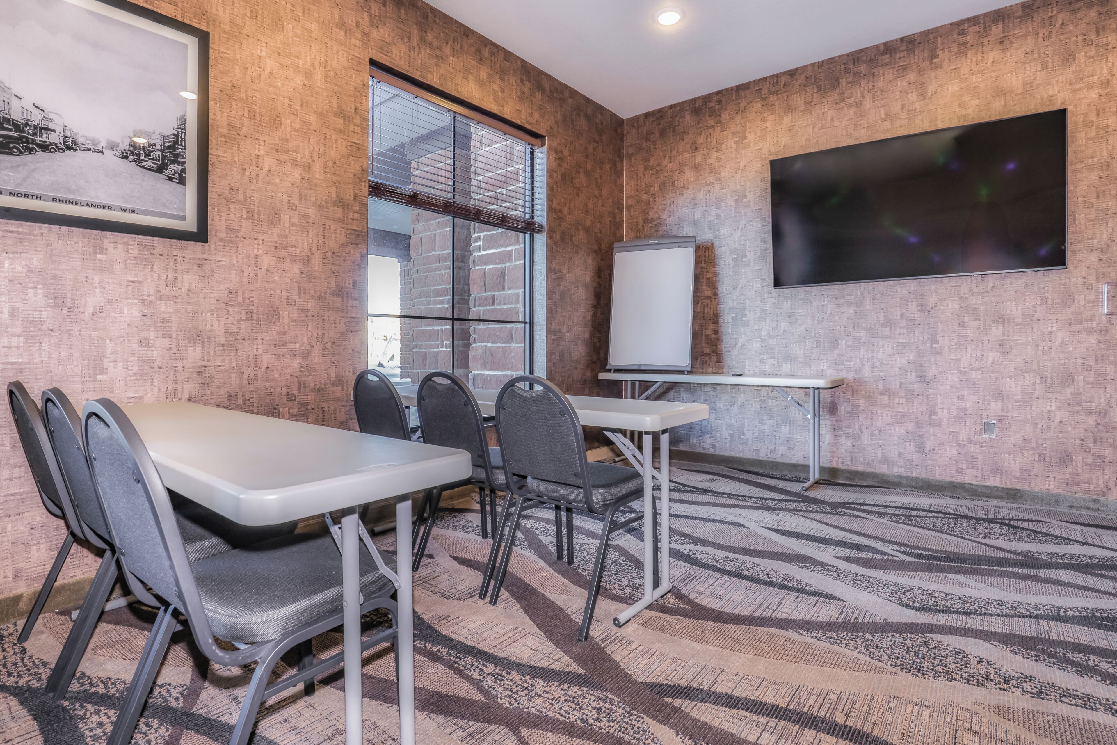 A conference room with a brick wall, a large window, a whiteboard, and a television.