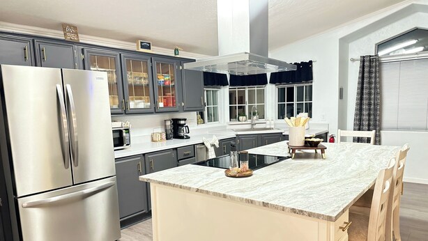 A modern kitchen with a stainless steel refrigerator, dark cabinets, and a marble island with a sink and stools. - Charming 3-bedroom house Peaceful wine country Home Near Sedona & Jerome (Clarkdale)