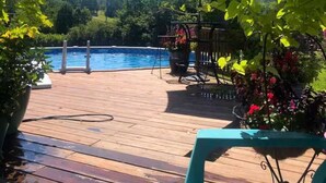 Une terrasse en bois avec une piscine, entourée de verdure et sous un ciel dégagé.