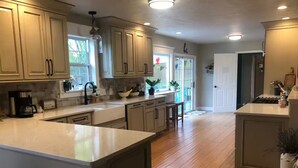 Une cuisine spacieuse avec des meubles de couleur bois clair, un îlot central et une grande fenêtre qui laisse entrer la lumière naturelle.
