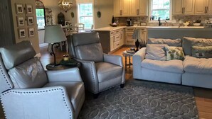 Un salon spacieux avec un canapé en cuir, un tapis à motifs et un coin repas agrémenté d’un lustre.