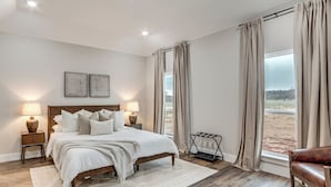 Ein Schlafzimmer mit einem großen Bett, zwei Nachttischlampen, Blick ins Freie und einem Vorhangfenster.