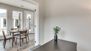 Ein moderner Essbereich mit Holztisch und -stühlen, einer Vase mit Pflanze und Blick ins Freie durch große Fenster.