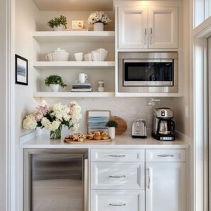 Una cocina con gabinetes blancos, microondas, cafetera y tostadora.