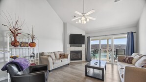 A modern living room with a fireplace, a ceiling fan, and a view of the outdoors.