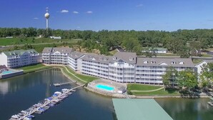A lakeside hotel with multiple buildings, a dock with boats, and a tower in the background.
