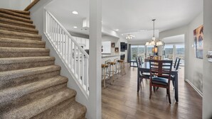 A spacious kitchen with modern appliances, a dining area with wooden chairs, and a staircase with carpeted steps.