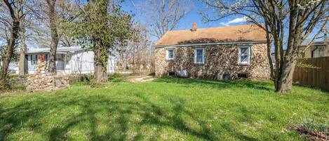 A stone house with a stone chimney, surrounded by a grassy yard and trees.