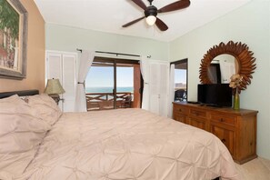Ein Schlafzimmer mit Bett, Deckenventilator, Kommode, Fernseher und Meerblick durch eine Schiebetür.
